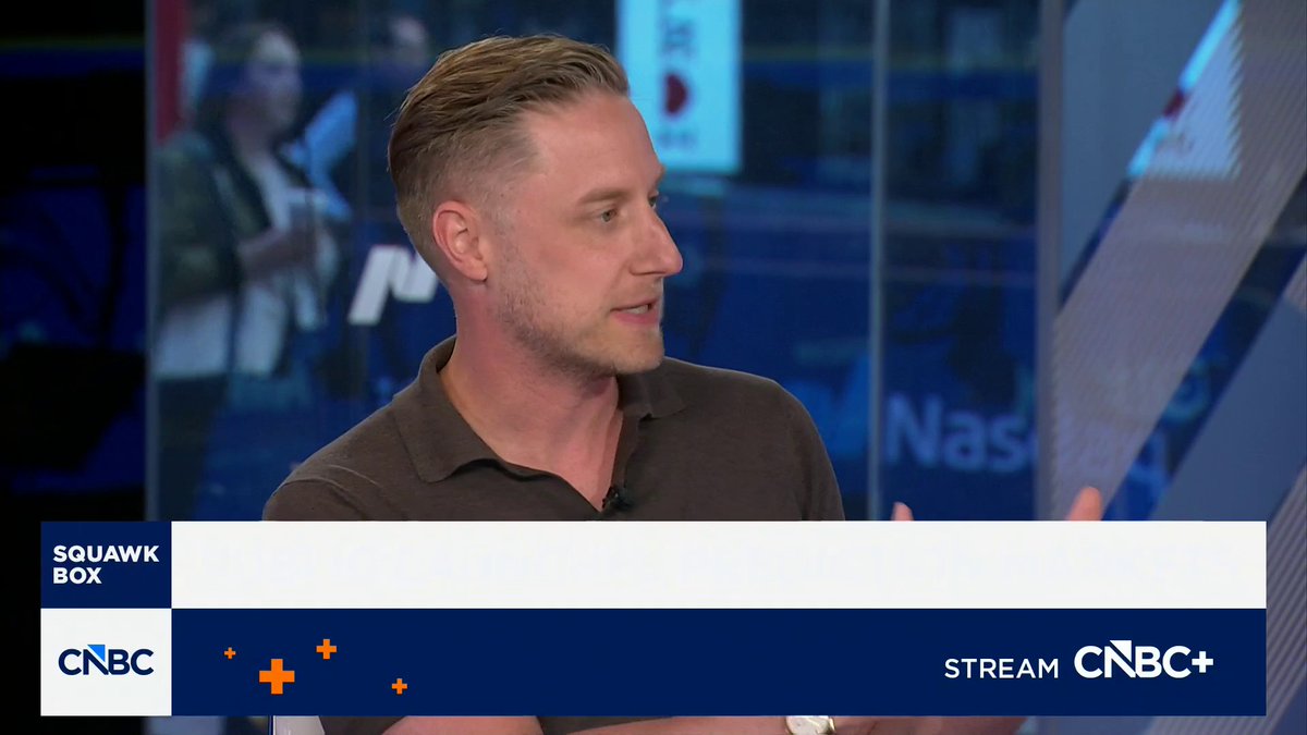 A CNBC Squawk Box segment showing a man with blonde hair in a brown polo shirt speaking in profile, with the Nasdaq visible in the background and a 'STREAM CNBC+' banner at the bottom.