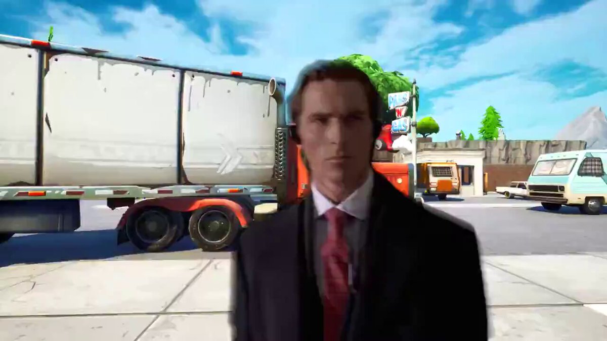 The image features a man dressed in a suit, standing next to a large white truck with red accents. He appears to be posing for a photo or video, possibly for a promotional or marketing campaign related to the truck. The background of the image includes other vehicles and buildings, suggesting that this scene takes place in an urban setting.