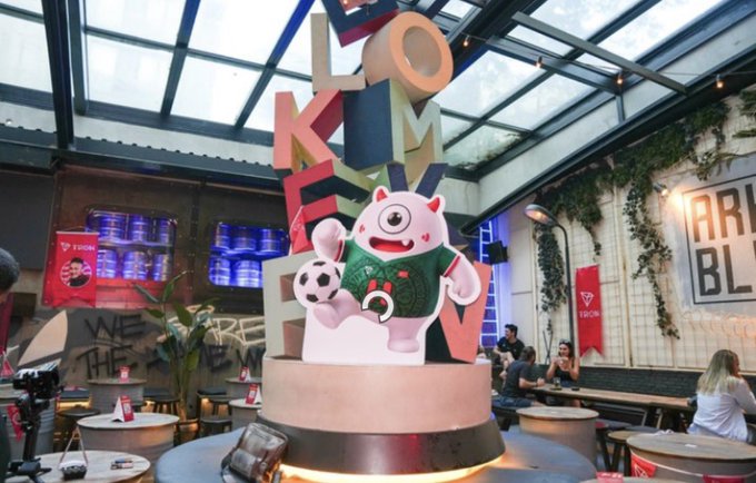 An indoor venue featuring a large decorative sculpture of a pink cartoon character holding a soccer ball, surrounded by large letters and a rooftop structure.