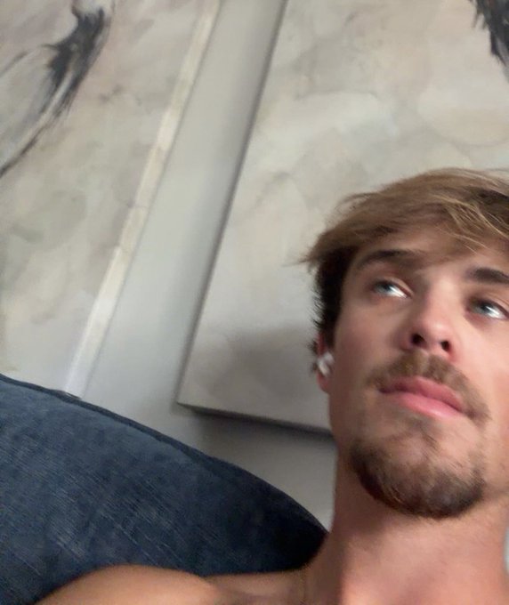 The image features a man with a beard wearing headphones, sitting comfortably on a couch or chair. He has his eyes closed while looking up at something above him. The photo appears to be taken from an unusual angle, as if someone took a selfie of him in this position. The caption provided seems to be related to the post about the man watching sui nuke but he can't move and is stuck in sui so he gets one wicked out of the short of sui.