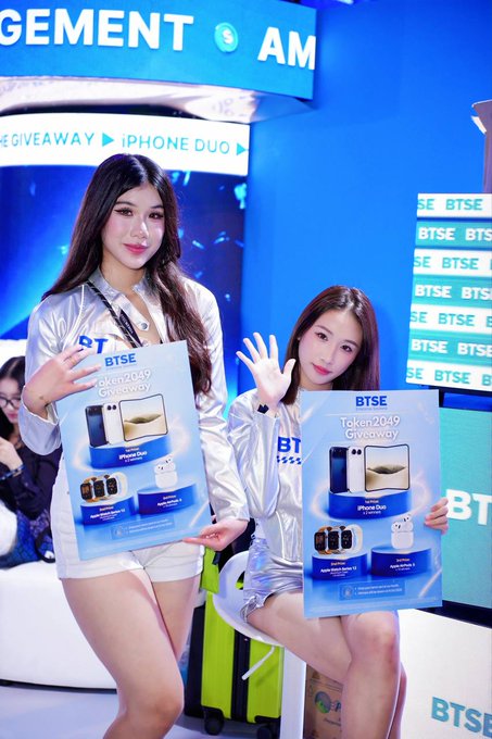 Two promotional models pose at the BTSE booth at Singapore's TOKEN2049 conference, holding signs advertising the "Token2049 Giveaway" featuring prizes like iPhone Duo, Apple Watch Series 10, and AirPods 4.

The accompanying post describes the BTSE booth as a lively highlight of TOKEN2049, featuring interactive elements, robots, and various giveaways including the iPhones and Apple products shown on the promotional signs in the image.