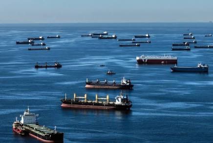 A vast fleet of cargo ships and tankers is anchored at sea, illustrating the massive scale of global shipping operations that blockchain platforms like @EthraShip aim to make more transparent.