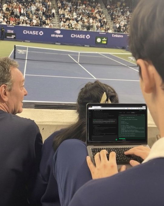 A developer uses Devin AI on a laptop while attending the US Open tennis tournament, with Chase and Emirates sponsor banners visible in the background, fitting the post's call for cool-location screenshots of the tool.