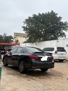A black sedan is being washed at home in a courtyard, with a person attending to the vehicle while it sits in front of a white SUV and a large green tree. The caption "this is how my weekend is starting" captures the leisurely start as the owner enjoys the convenience of a "car washer at home" service.