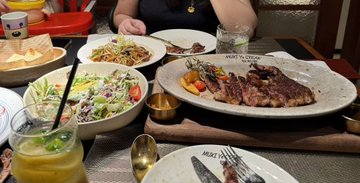 A restaurant table set with various dishes, including a salad, a steak dish with garnish, bread, and a glass of orange juice.
