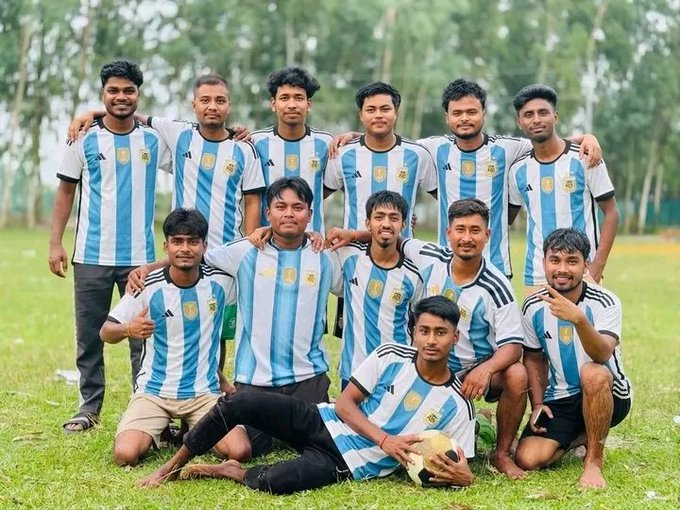 A group photo of a soccer team wearing blue and white striped Argentina-style jerseys, posing on a grassy field with a soccer ball.