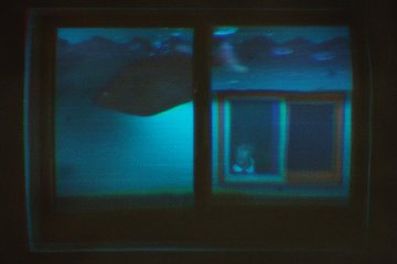 A dark view through a window showing a dimly lit scene with blue and green lighting and what appears to be a small figure inside.