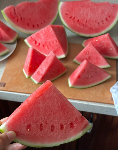 Several slices of red watermelon are arranged on a table, with one triangular slice held up in the foreground.