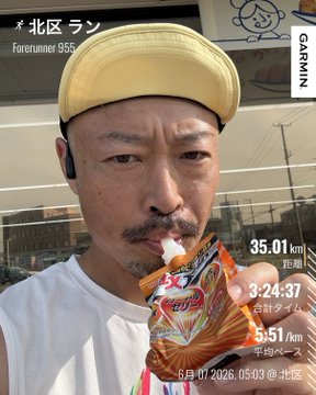 The image features a man wearing a yellow baseball cap, holding an orange sports drink with a straw in his mouth while standing outside of a building. The caption for the image reads "おはよー 今日はLSD ろんぐすろーだいえっと #STEPN". This suggests that the man is participating in an outdoor event or activity, possibly related to sports or fitness, and he has brought a sports drink with him for hydration.