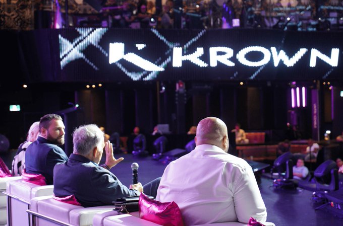 A panel of judges sits on a white leather sofa facing a stage, with the word 'KROWN' illuminated on a large screen behind them.