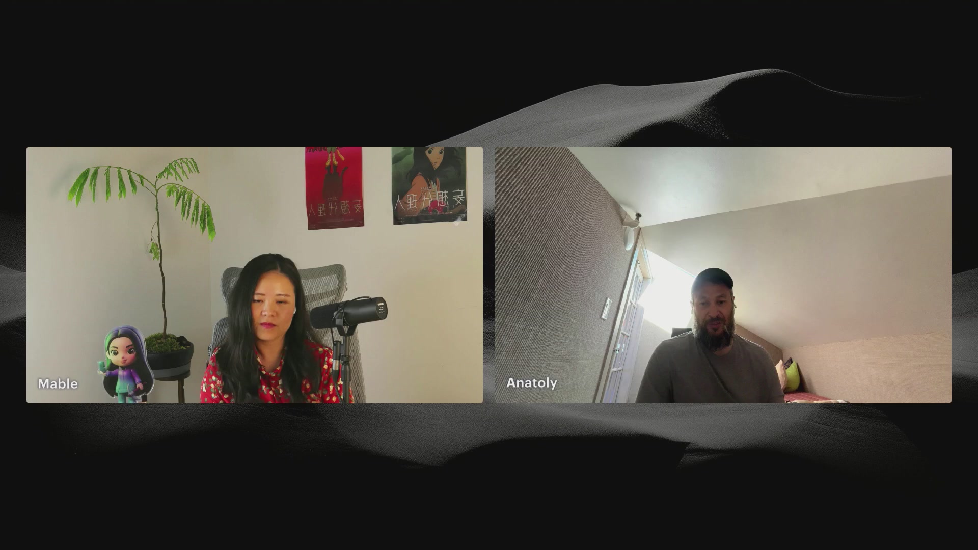 The image shows a man and woman sitting across from each other, having a video call using their laptops. They are both looking at the camera, engaging with one another through the screen of their devices. The background features a wall that has a poster hanging on it, adding an element of personalization to the space where they are connected.