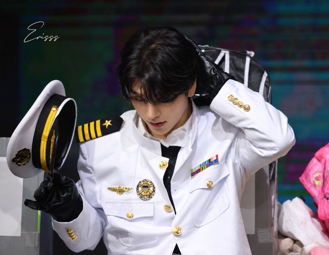 A young man in a white military-style dress uniform with gold buttons and a navy captain's hat is photographed with the watermark 'Erisss' in the top left.