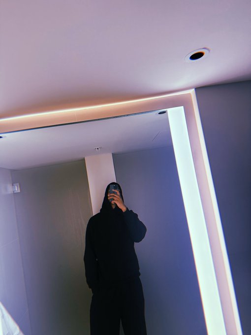 A mirror selfie of a person in a black hoodie taking a photo in a modern room with LED lighting.