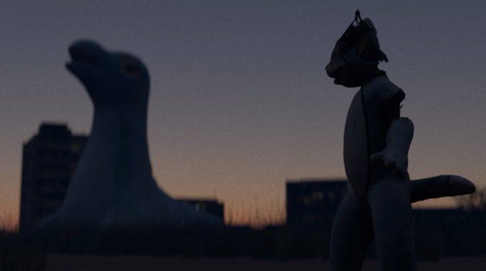 A twilight silhouette scene featuring a large seal or sea lion statue and a humanoid dinosaur-like figure against an orange and purple sunset sky with buildings in the background.