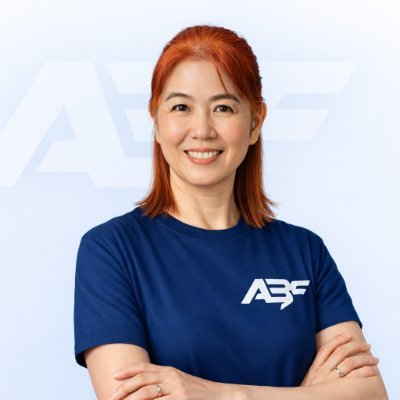 A smiling woman with red hair, wearing a navy blue t-shirt featuring the "ABF" logo, stands with crossed arms against a backdrop displaying the same ABF branding.

The image aligns with the post by depicting Helen Liu, the former Bybit Co-CEO now leading AB Finance (@abf_finance), as referenced in the caption discussing her new crypto finance venture.