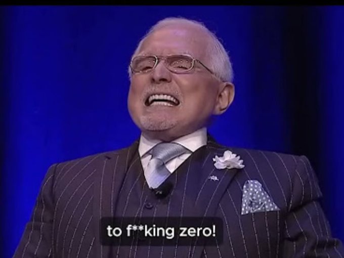 An older man with glasses and a gray beard, wearing a pinstriped suit, laughs against a blue background, with the subtitle reading 'to f**king zero!'.