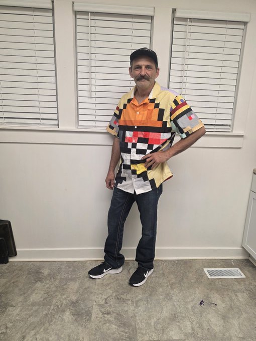 A man with a mustache and baseball cap poses indoors wearing a colorful geometric-patterned shirt and jeans, ready to head to DDNYC and NFT NYC with @doginaldogs as shown in the post.