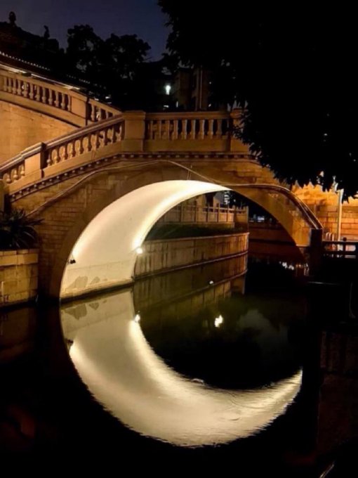 The arched bridge at night perfectly reflects in the water below, creating a beautiful "moon bridge" effect.