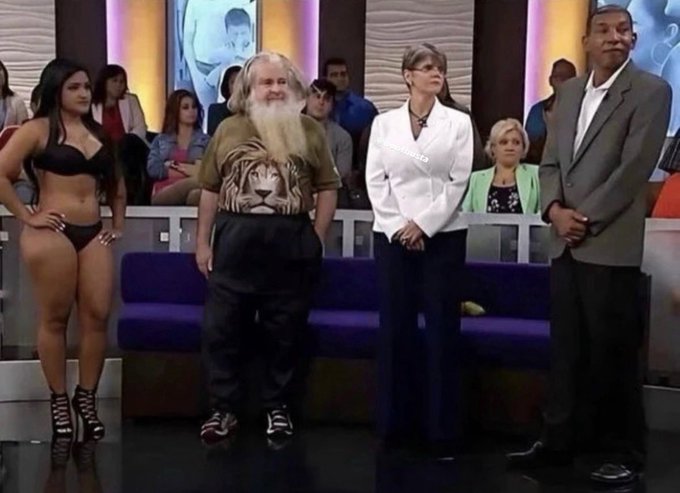 A still from a television talk show featuring four guests standing on stage: a woman in a black two-piece outfit, a bearded man wearing a tiger-print shirt, a woman in a white blazer, and a tall man in a gray suit, with an audience visible in the background.