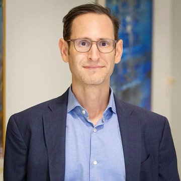 A man with glasses, wearing a blue shirt and dark blazer, smiles at the camera in a professional portrait, likely Matthew Sigel of VanEck, whose commentary on Strategy's Bitcoin sales as a "newspaper headline bottom" accompanies the image.