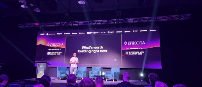 A wide shot of an 'ETHSOFIA' conference stage where a speaker presents in front of screens reading 'What's worth building right now' and 'SUI ENDURANCE: 2025 BLOCKCHAIN CONFERENCE.'