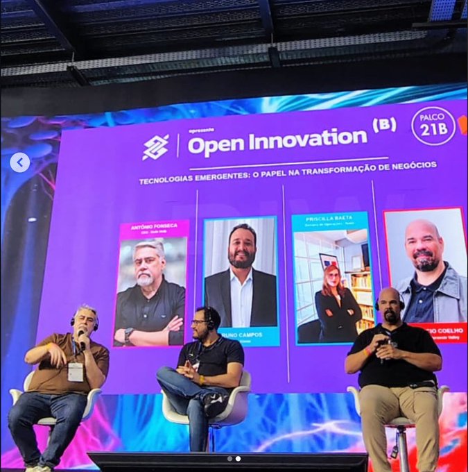 A panel discussion on stage at the "Open Innovation" event (Palco 21B), featuring speakers Antônio Fonseca, Bruno Campos, Priscilla Bata, and Rodrigo Coelho, discussing "Tecnologias Emergentes: O Papel na Transformação de Negócios" (Emerging Technologies: Their Role in Business Transformation). The image visually supports the post's message by capturing a live exchange of ideas between industry experts, illustrating how human collaboration drives meaningful technology adoption.