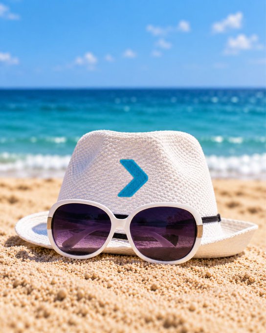A white straw fedora hat with a blue chevron logo and white-framed sunglasses with purple lenses sitting on sandy beach with the ocean in the background.