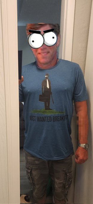A mirror selfie of a man wearing a blue t-shirt that says 'JUST WANTED BREAKFAST' with an illustration of a suited figure, with a cartoonish wide-eyed face drawn over his head.