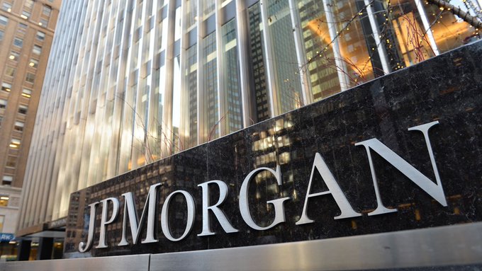 A polished black granite sign displays the "JPMORGAN" logo in silver lettering, mounted outside a tall glass office building.