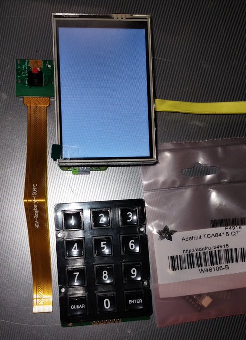 An Adafruit TCA8418 I2C keypad and a TFT display component laid out on a surface, with the display showing a blue screen and the packaging visible.