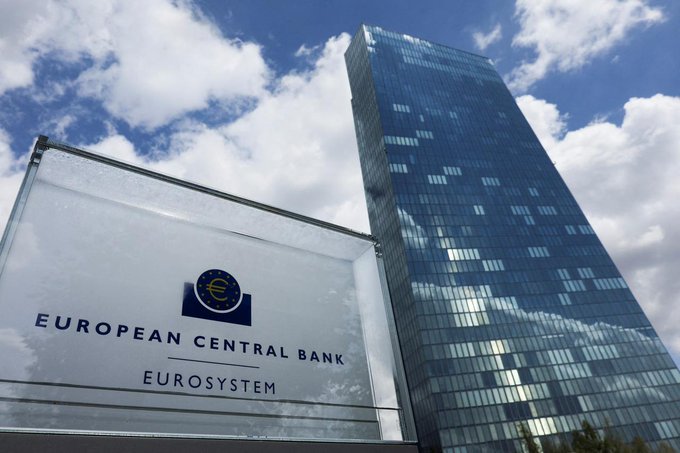 The European Central Bank (ECB) skyscraper in Frankfurt, shown alongside its sign reading 'EUROPEAN CENTRAL BANK EUROSYSTEM' against a partly cloudy sky.