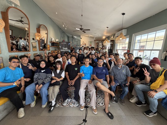 A lively group of young tech enthusiasts and mentors pose together inside a cozy, mirror-lined cafe, smiling and flashing peace signs at the camera, with a "Trade everything." promotional banner for TradingView visible in the background. The image captures the warm, collaborative energy of a community meetup, perfectly matching the upbeat post about enjoying the vibe.