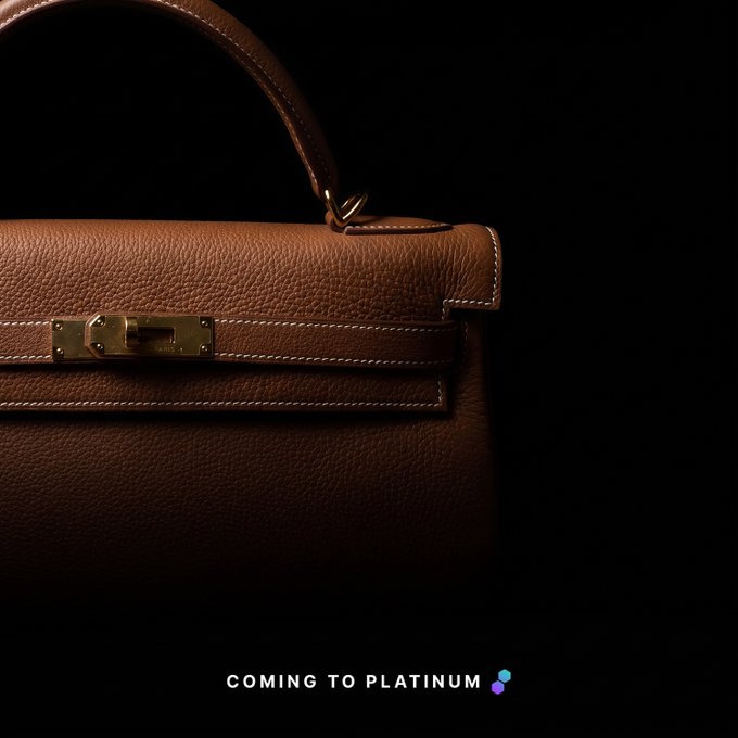 A close-up product shot of a tan leather Hermès Kelly bag with gold hardware against a black background, with text reading 'COMING TO PLATINUM' and a small purple logo.