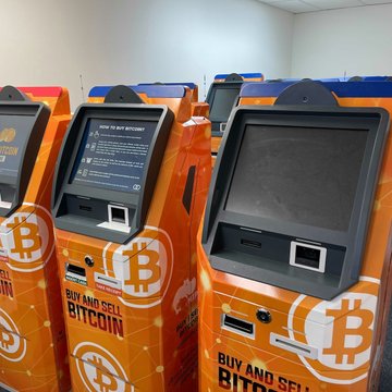 A lineup of orange Bitcoin ATMs displays "BUY AND SELL BITCOIN" along their sides, illustrating the type of machines now subject to Alabama's new crypto ATM fraud law that took effect October 1.
