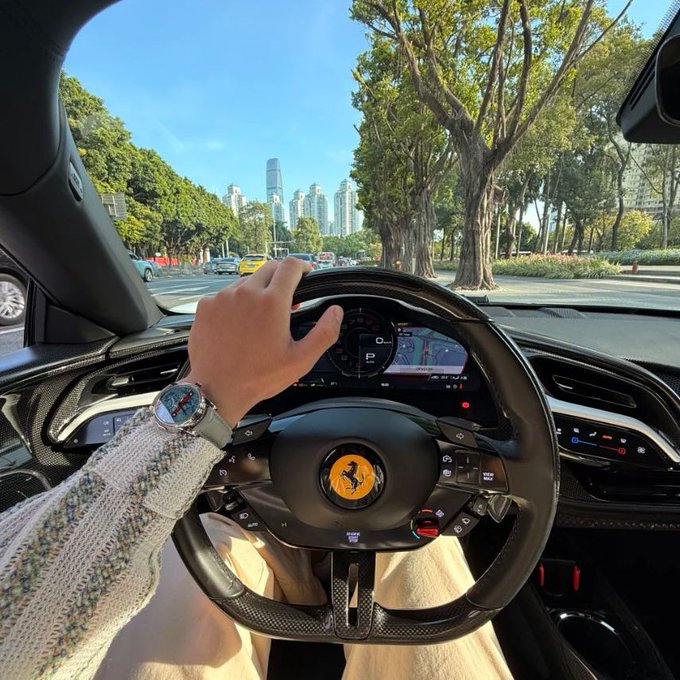 A driver grips the steering wheel of a Ferrari, identifiable by its iconic prancing horse logo, while cruising down a tree-lined city boulevard with skyscrapers in the distance. The image evokes the thrill and risk-taking mindset the post warns against—chasing high stakes like a luxury supercar without proper strategy—reflecting how new crypto futures traders often risk their entire capital on a single bet, only to lose everything in one wrong move.