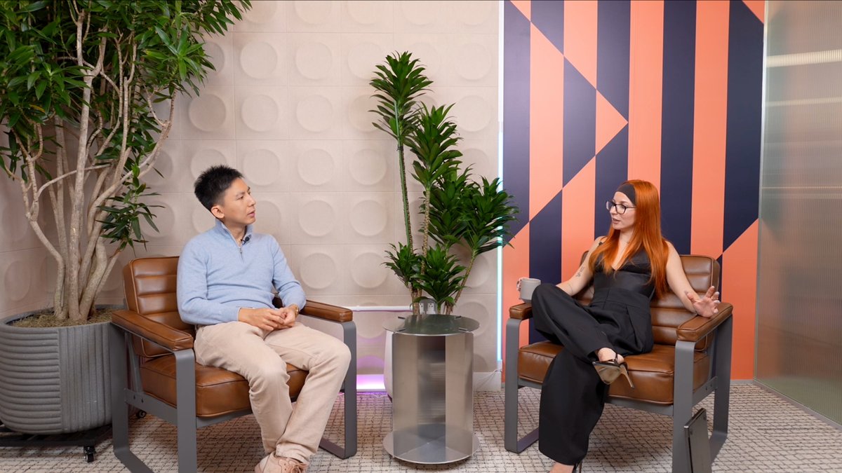 Two people sit in tan leather chairs having a conversation in a modern, plant-filled setting—one in a light blue sweater, the other in a black outfit with long red hair—capturing the interview setting referenced in the post, which announces a discussion with David Gan of Inception Capital about automated finance, founder conviction, and emerging markets.
