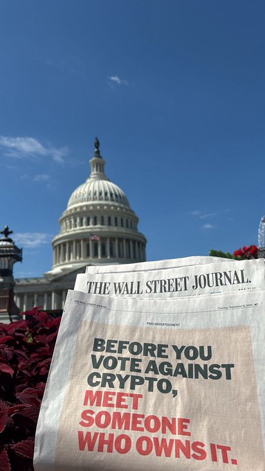 A copy of the Wall Street Journal is held up in front of the U.S. Capitol building, featuring a paid advertisement from the National Cryptocurrency Association of America titled "Before You Vote Against Crypto, Meet Someone Who Owns It." The ad, promoting support for the CLARITY Act ahead of a September 15th vote, is shown alongside red flowers with the iconic Capitol dome in the background.