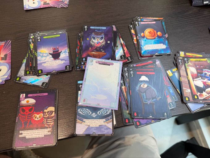 A tabletop display of trading cards featuring colorful fantasy characters with various abilities, numbers, and effect text arranged on a dark surface.