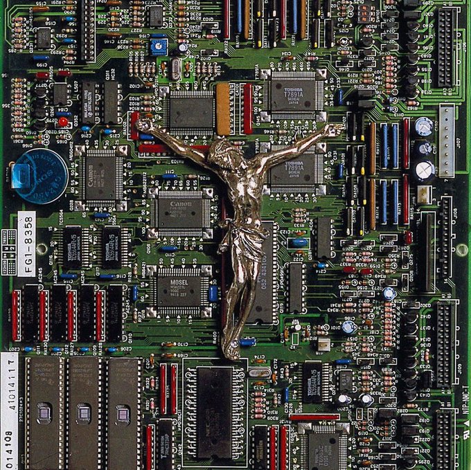 A silver crucifix rests atop a green computer motherboard filled with electronic components, with a label reading 'FG1-8358'.