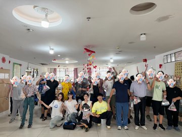 A large group of people wearing face masks poses for a photo in a brightly lit room decorated with red and gold Chinese ornaments.