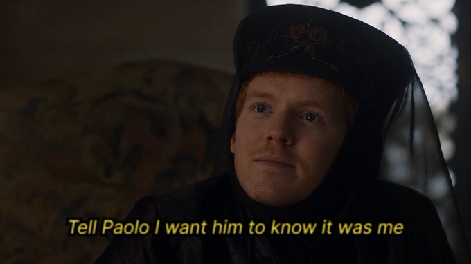 A scene from a TV show featuring a character in a black hooded outfit, with the subtitle "Tell Paolo I want him to know it was me."