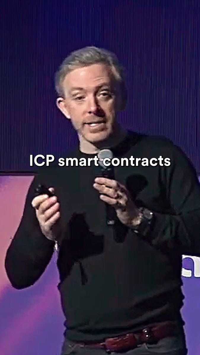 The image features a man standing behind a microphone, speaking into it during an event or presentation. The background includes text that reads "ICP Smart Contracts" and "focus on what is in the image and how it relates to the post". This suggests that the speaker might be discussing the topic of smart contracts and their significance in the context of the ICP presentation.

The man's attire consists of a black sweater, which contrasts with his dark hair color. The microphone he holds is positioned close to him, indicating that he is actively engaged in delivering his speech or presentation.