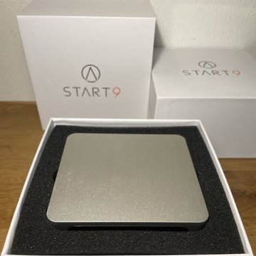 A product photo showing a silver/metallic square hardware device (likely a hardware wallet) in foam packaging inside a white box labeled 'START9' with a matching branded outer box behind it.