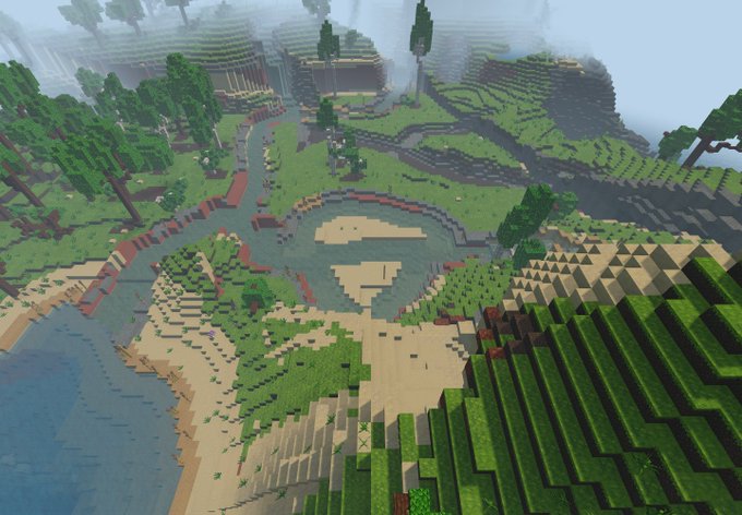 A wide aerial view of a Minecraft world showing a blocky landscape with green hills, trees, a river, sandy shores, and large terraced mountains in the distance under a hazy sky.