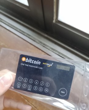 A close-up of a hand holding a Bitcoin-branded 'One Time Password Card' by Mt.Gox with a numeric keypad.
