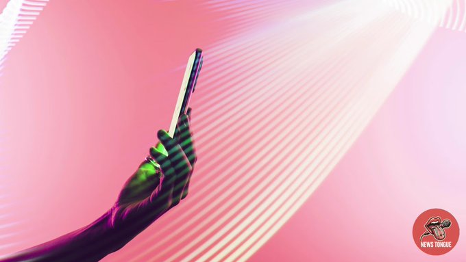 A hand holds a smartphone against a pink background with light streaks, with a 'NEWS TONGUE' logo in the corner.