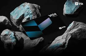 The image features a black Visa card laying flat on top of some rocks. The rock formation includes gray and blue stones that are scattered around the card. The background of the image is dark, which contrasts with the vibrant colors of the card and the rocks. The text in the image reads "Meet 𝐛𝐨𝐞𝐬𝐚𝐥𝐦𝐧𝐢𝐨𝐯𝐡" (Trade), indicating that the card is associated with a trade platform, while "Trade 𝐀𝐨𝐜𝐭𝐥𝐨𝐮𝐬" (Spend) suggests that users can spend money on this platform. The text also mentions "Earn all from a single app that's already live in 150+ countries!" which implies the card is available for use worldwide, and it has been launched recently.