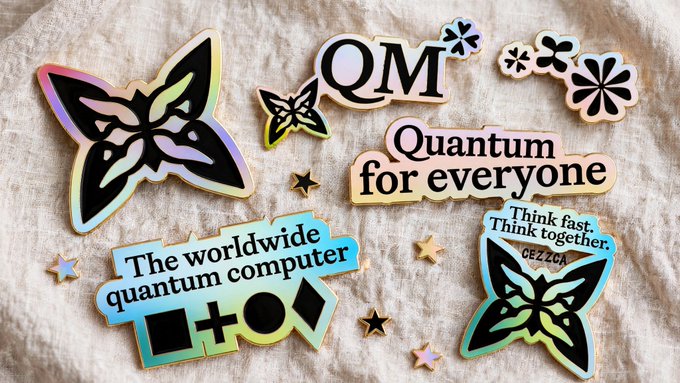 A collection of holographic, iridescent stickers laid on a beige fabric surface, featuring butterfly motifs, stars, and text reading "QM," "Quantum for everyone," "The worldwide quantum computer," and "Think fast. Think together. CEZZOA." The stickers visually represent Quip's quantum messaging app branding, aligning with the post about Quip showcasing its product at QuantumTech World 2026 in Boston.