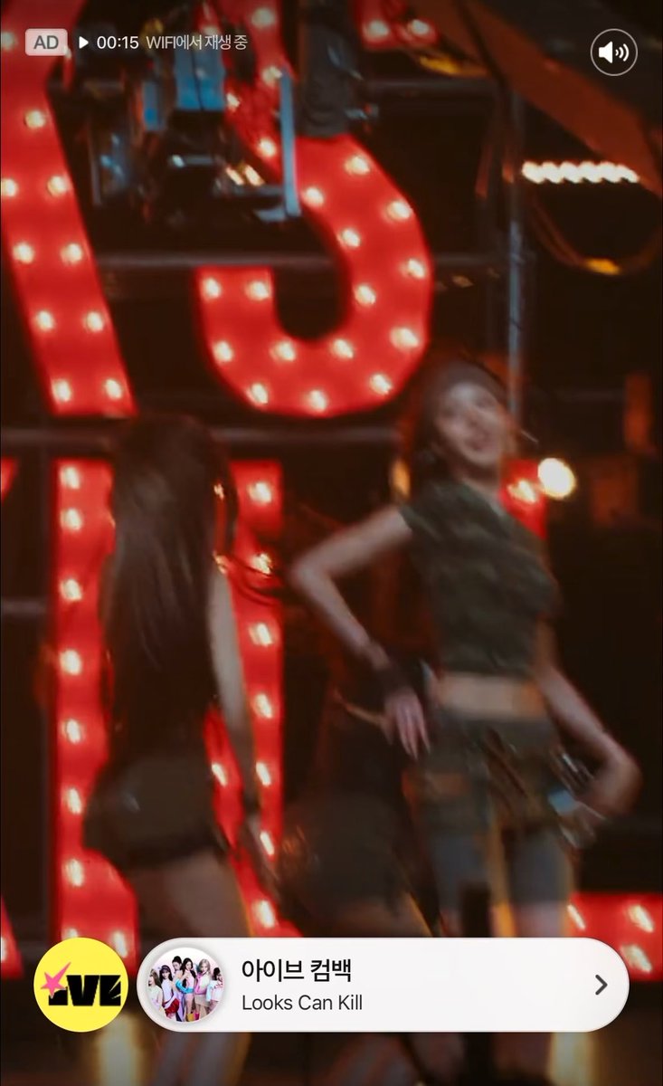 A screenshot from a music video or advertisement featuring two women dancing in front of large illuminated red letters, with Korean text and the song title 'Looks Can Kill' by IVE visible at the bottom.