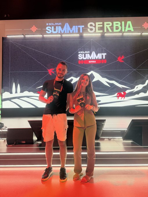 Two people pose on stage at the Solana Summit Serbia event, with a large screen displaying the event branding behind them.